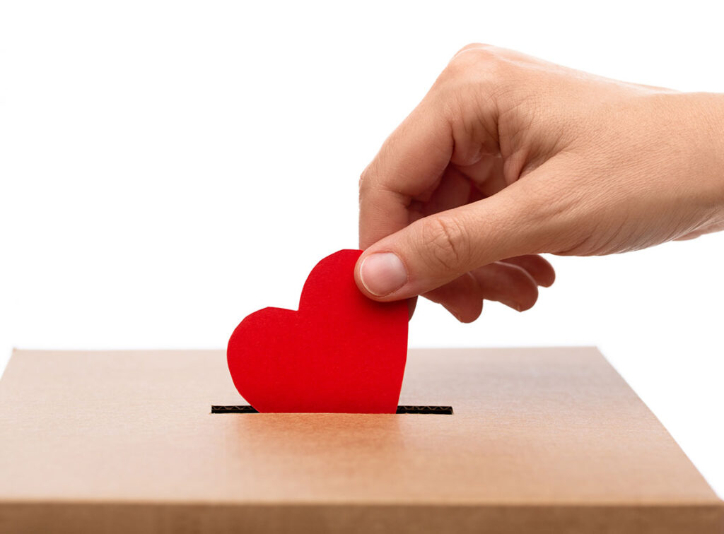 person dropping red paper heart into charity donation box